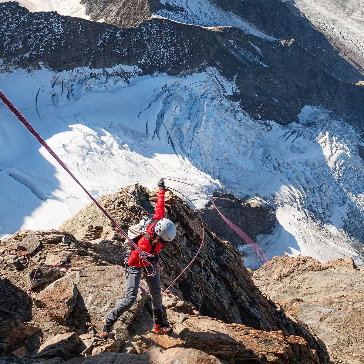 A female climber rappelling down a cliff in Schreckhorn, Switzerland. Wearing the Stelar Equipment Ultralight Down Jacket in Red.