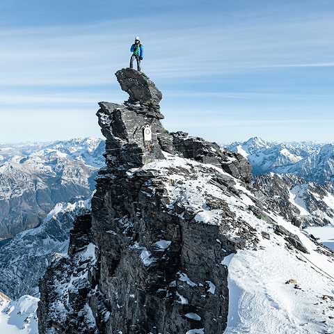 An alpinist standing on a sharp summit in Gross Spannort, Switzerland. Wearing the Stellar Eq Hyperlight Down Hood in Blue.