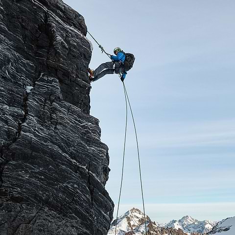 An alpinist repelling down a rock in Gross Spannort, Switzerland. Wearing the Stellar Equipment Hyperlight Down Hood in Blue.