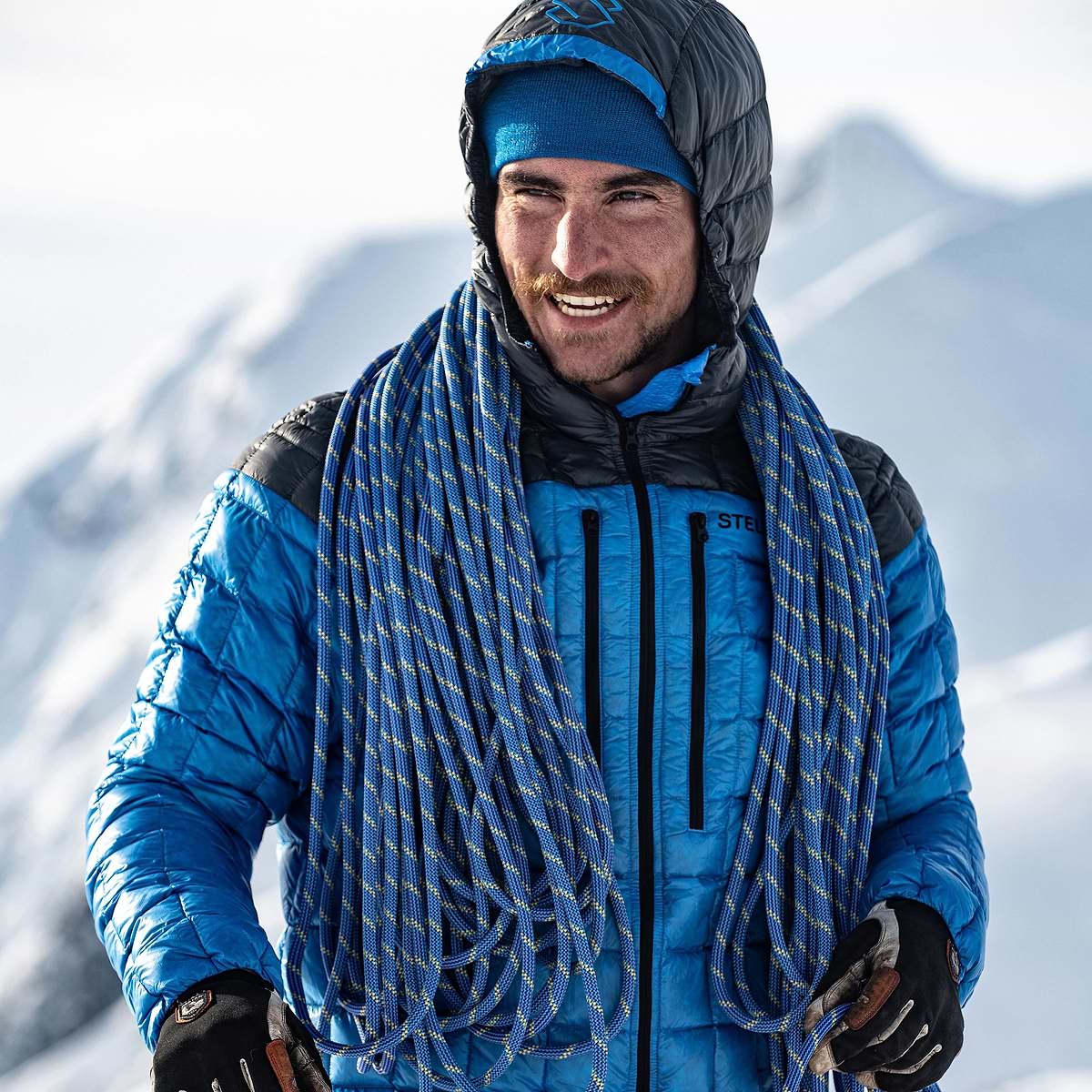 Adrien Grabinski standing on a sunny mountain top in Terrace, Canada wearing the Stellar Equipment Hyperlight Down Hood in Blue.