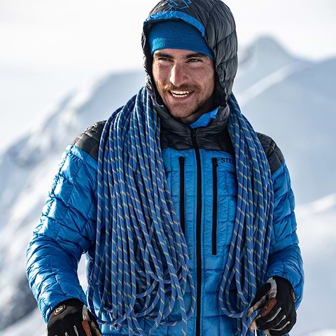 Adrien Grabinski standing on a sunny mountain top in Terrace, Canada wearing the Stellar Equipment Hyperlight Down Hood in Blue.