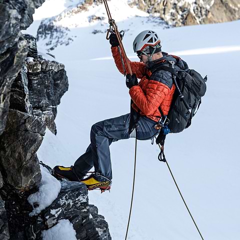 A mountaineering guide repelling down a rock face on Gross Spannort in Switzerland, wearing the Stellar Equipment Mens Hyperlight Down Hood in orange.