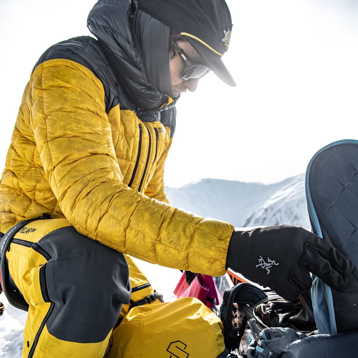 Tanner Elliott placing his skins in his backpack on a summit in Terrace, Canada. Wearing the Stellar Eq Hyperlight Down Hood in yellow.