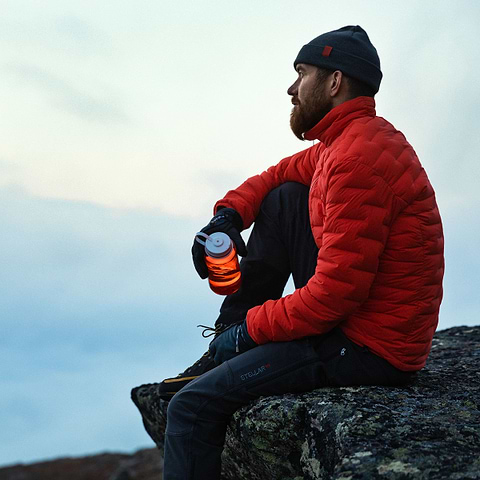 David Kantermo sitting on a rock, enjoying the view in Åre, Sweden. Wearing the Stellar Equipment Stretch Down Jacket 2.0 in Orange.