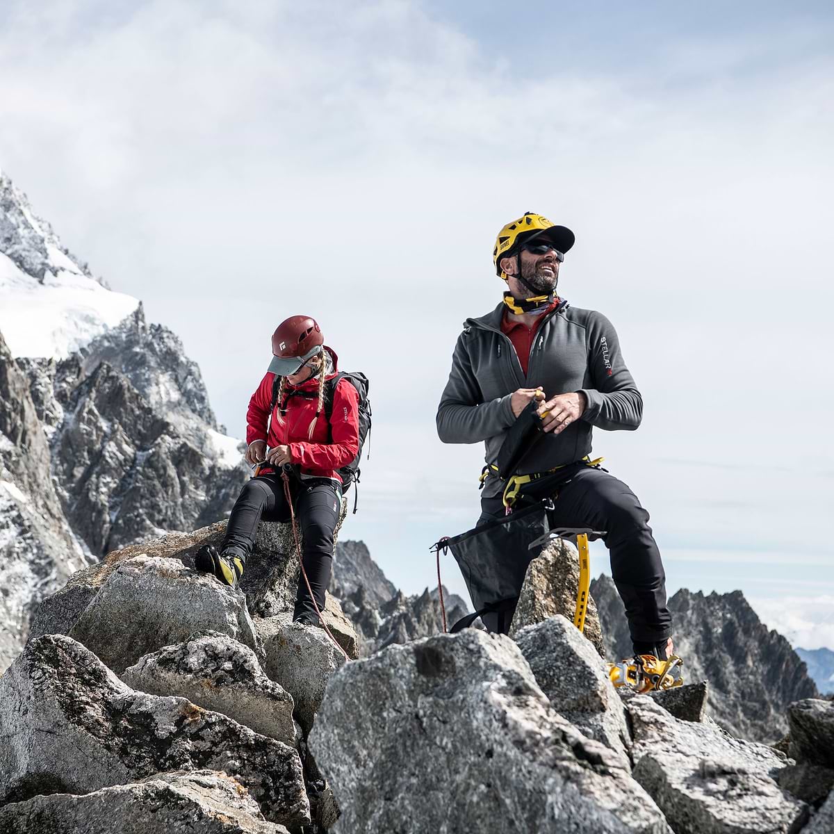 Two hikers checking their gear on a summit. Wearing the Stellar Equipment Softshell Pants in dark grey.