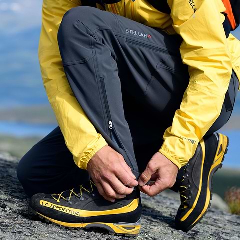 A hiker is closing his leg zip so he can have his Stellar Equipment Softshell Pants in grey over the boots.