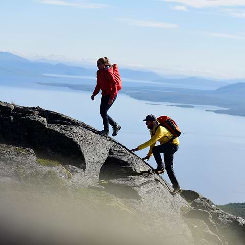 Two hikers reaching a summit with a big lake in the background. Both wearing the Stellar Equipment Softshell Pants in grey.