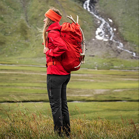 A female hiker is standing in a valley in Björkliden, Sweden. Wearing the Stellar Equipment Ultralight Shell Jacket in red.