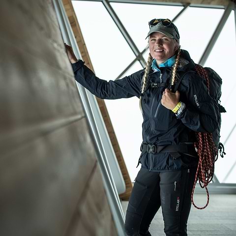 A woman preparing to hike on the mountain, wearing the Stellar Equipment Ultralight Shell Jacket in Dark blue.
