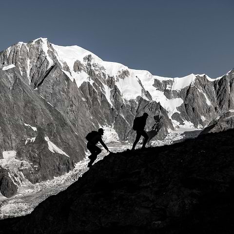 Two silhouettes hiking with a big mountain in the background.