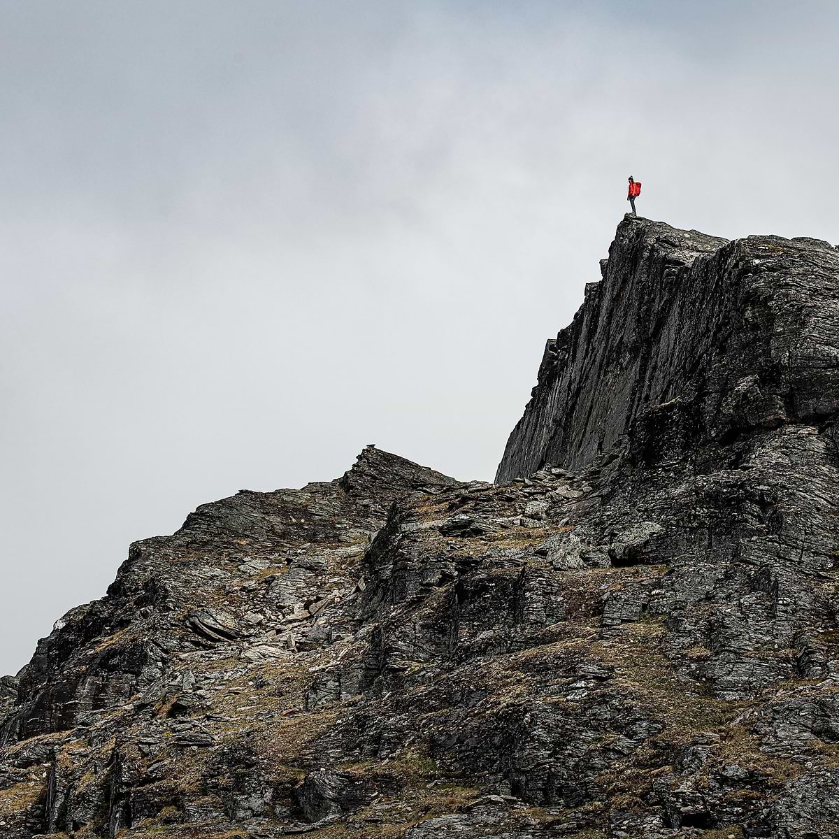A female hiker is standing on a sharp summit in Björkliden, Sweden. Wearing the Stellar Eq Ultralight Shell Jacket in red.