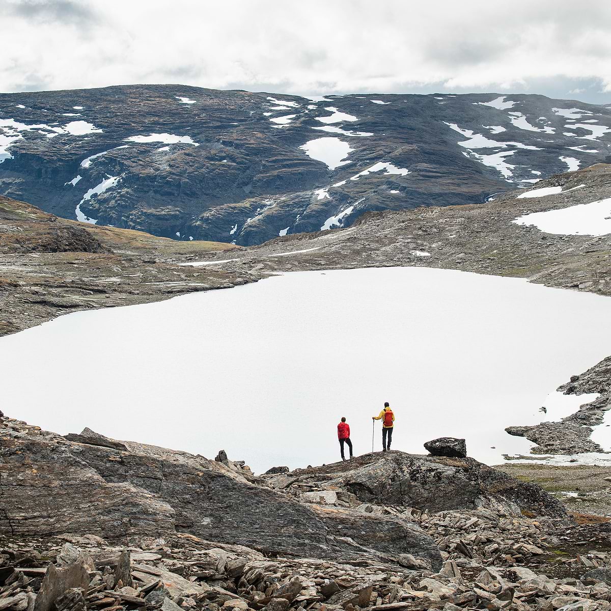 Two hikers standing by a frozen lake in Björkliden, Sweden. Both wearing the Stellar Equipment Ultralight Shell Jacket in red and yellow.