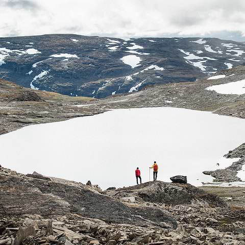 Two hikers standing by a frozen lake in Björkliden, Sweden. Both wearing the Stellar Equipment Ultralight Shell Jacket in red and yellow.