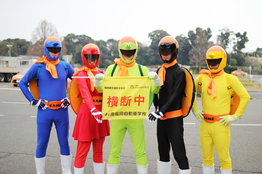 ▼かめライダー 南福岡自動車学校のイメージキャラクター。交通安全のヒーローとして中学校や高校の自転車安全講話や横断歩道の旗振り活動、企業の交通安全研修等を行っている。活動の幅が広がり「かめライダーず」として5色に分かれた。決めゼリフは「幸あれ！」。